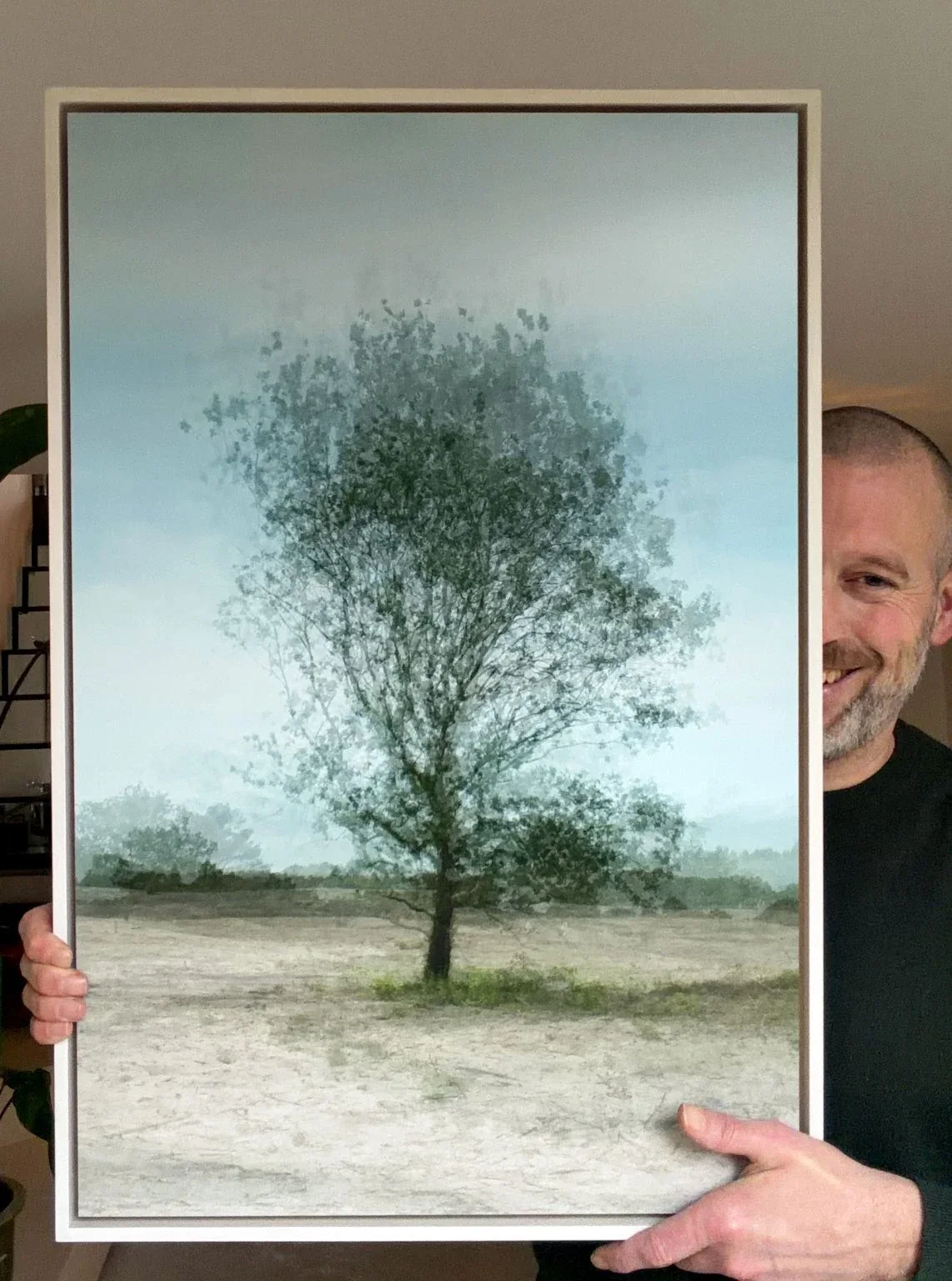 Franklin houdt een werk uit Mapping van Kim Boske vast: een boom op de heide, opgebouwd uit vele opnames, in een witte lijst.